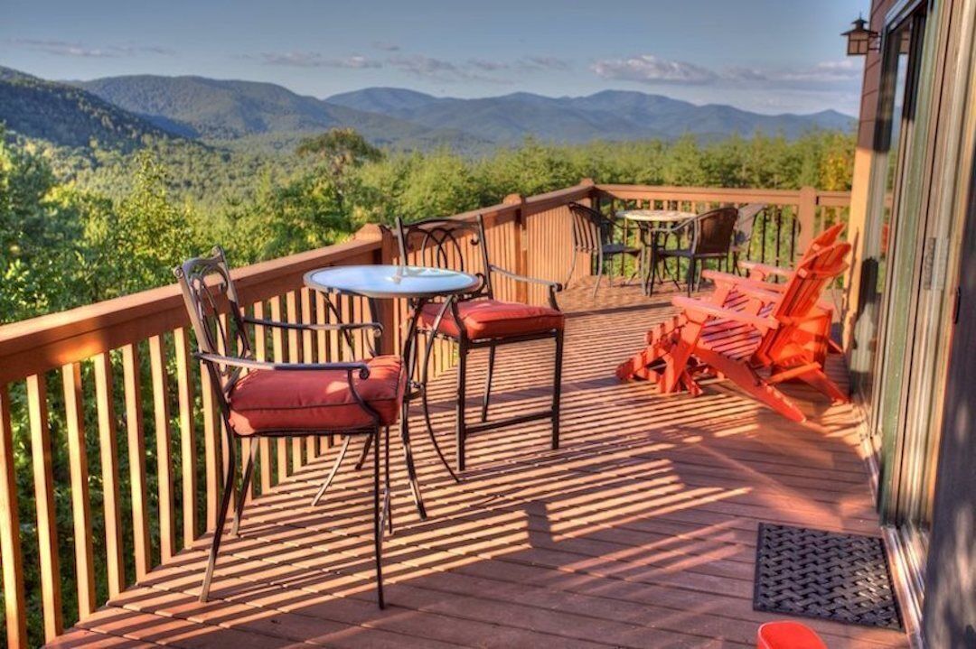 Une terrasse en bois, aménagée avec du mobilier d’extérieur, notamment des chaises et une table, qui offre une vue sur un paysage montagneux.
