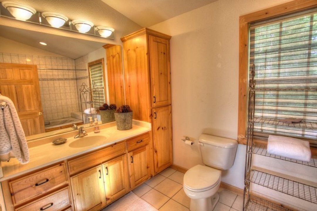 A bathroom with wooden cabinets, a sink, a toilet, and a window with blinds.
