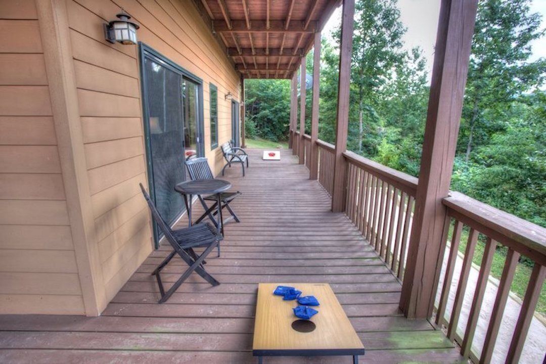 A wooden deck with a table and chairs, a covered area with a railing, and a view of trees.