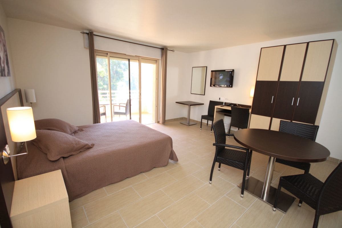 A hotel room with a bed, a desk, a chair, a TV, and a wardrobe.