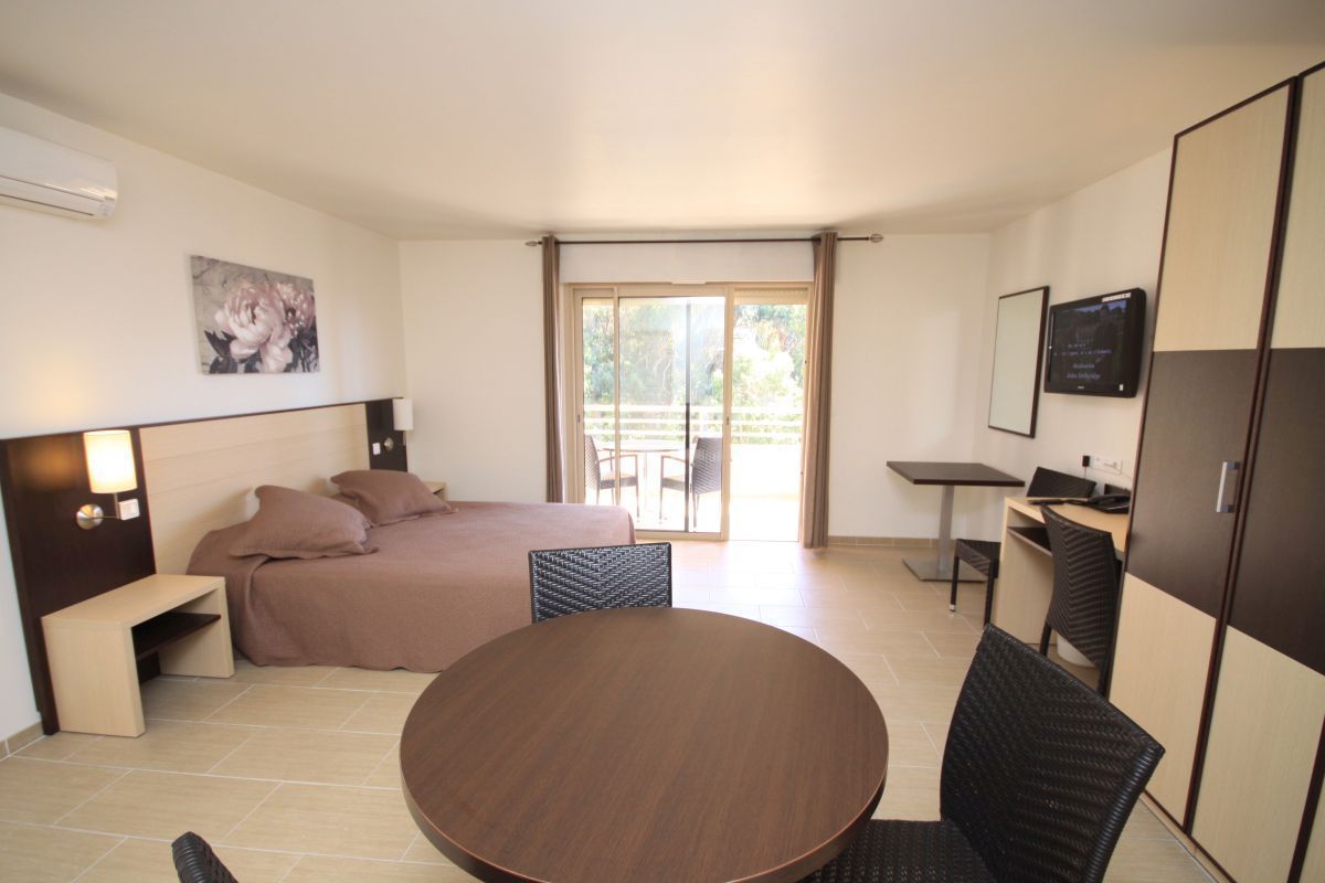 A modern hotel room with a bed, a dining table, a desk, and a TV.
