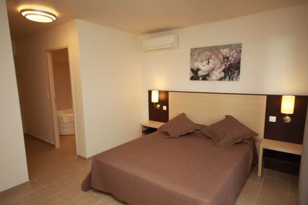 A hotel room with a single bed, bedside lamps, a painting on the wall, and a door leading to another room.