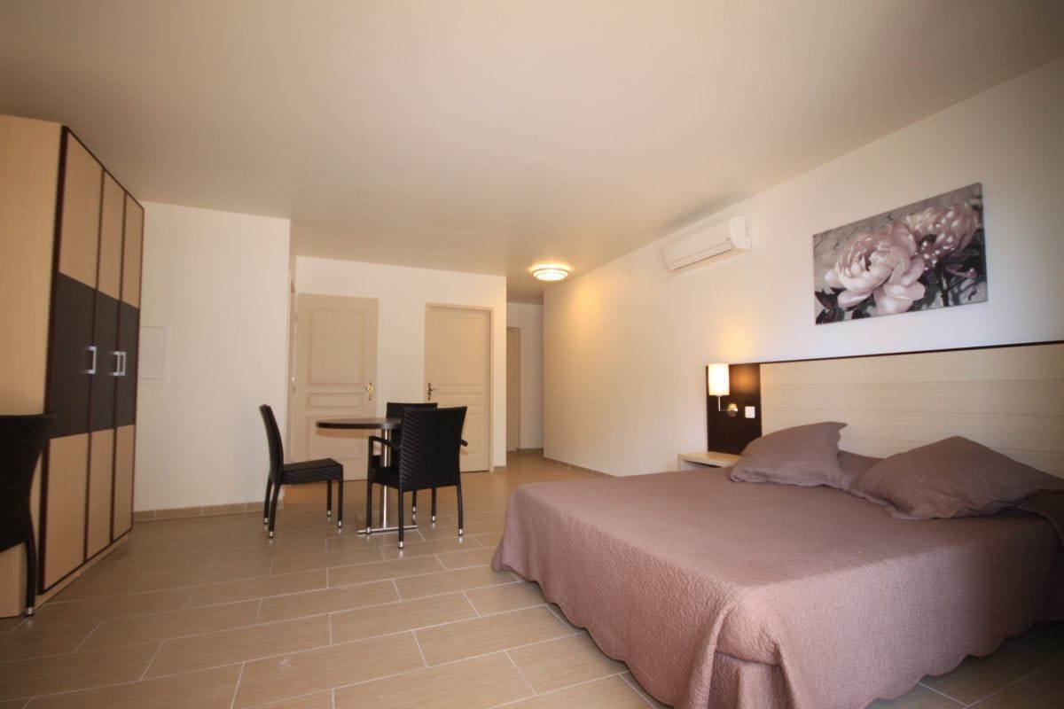 A bedroom with a bed, a desk, and a chair. There is a door in the background.