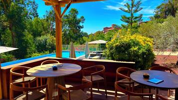 Un patio al aire libre con muebles de madera, piscina y abundante vegetación.