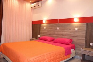 Une chambre d’hôtel avec un lit, des tables de chevet, une tête de lit en bois et un mur d’accent rouge.