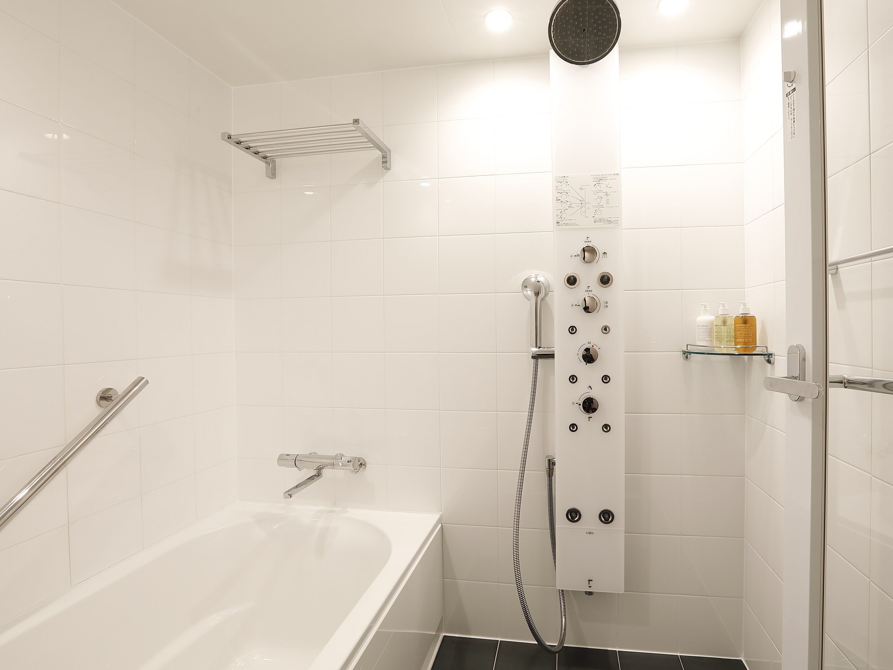 A modern bathroom with a bathtub, a shower with multiple controls, and a glass shelf with toiletries.