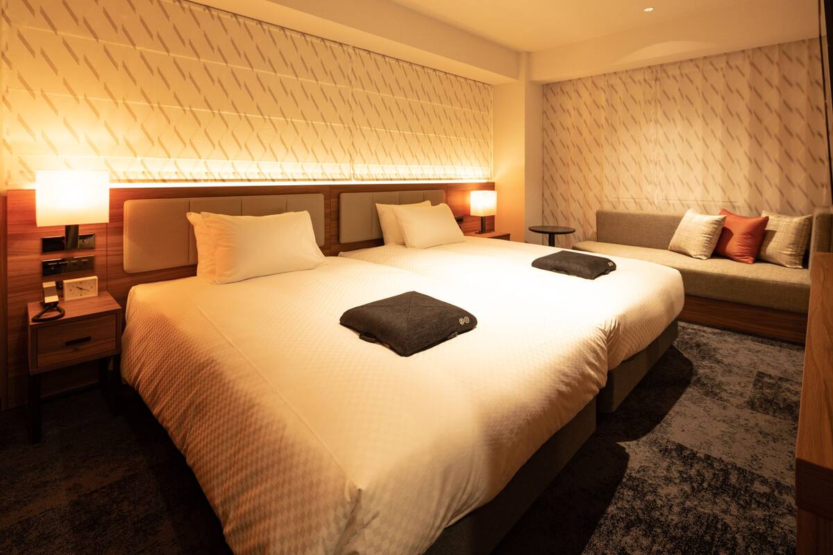 A hotel room with a large bed, two bedside tables, a nightstand, a sofa, and a patterned wall.