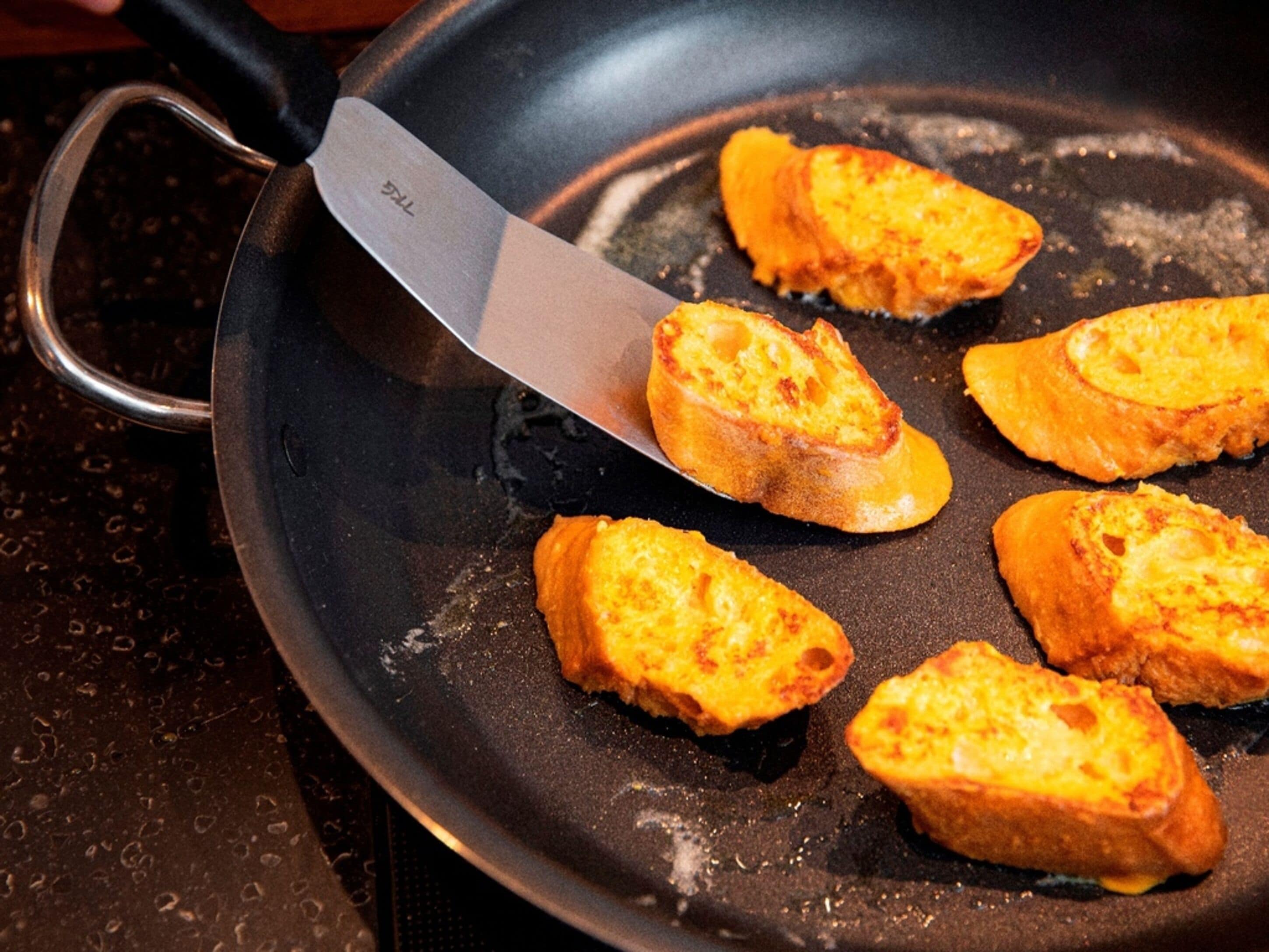 Una sartén con un cuchillo y varias rebanadas de pan cocinándose.