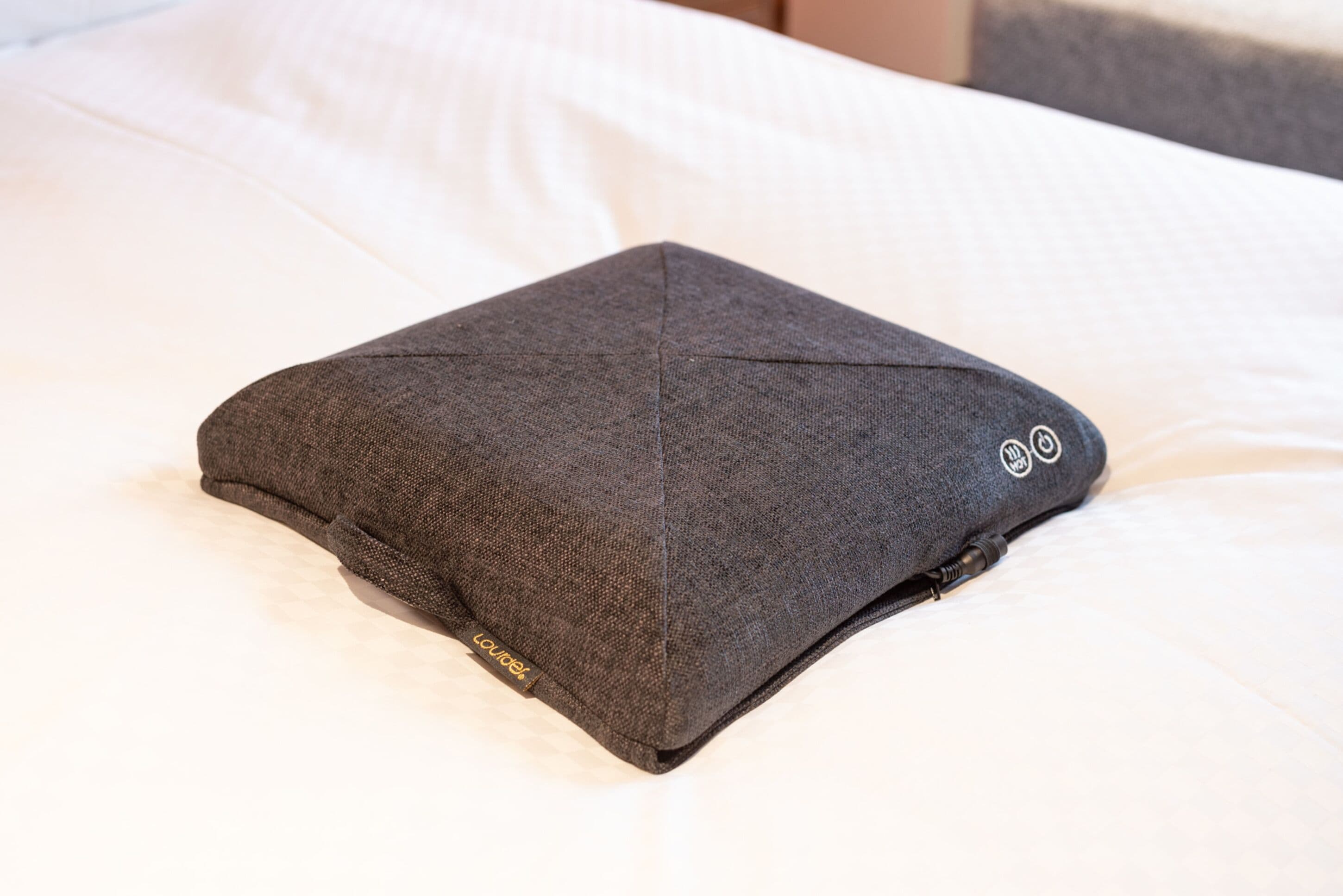 Um travesseiro escuro e bem dobrado sobre uma cama com roupa de cama branca.