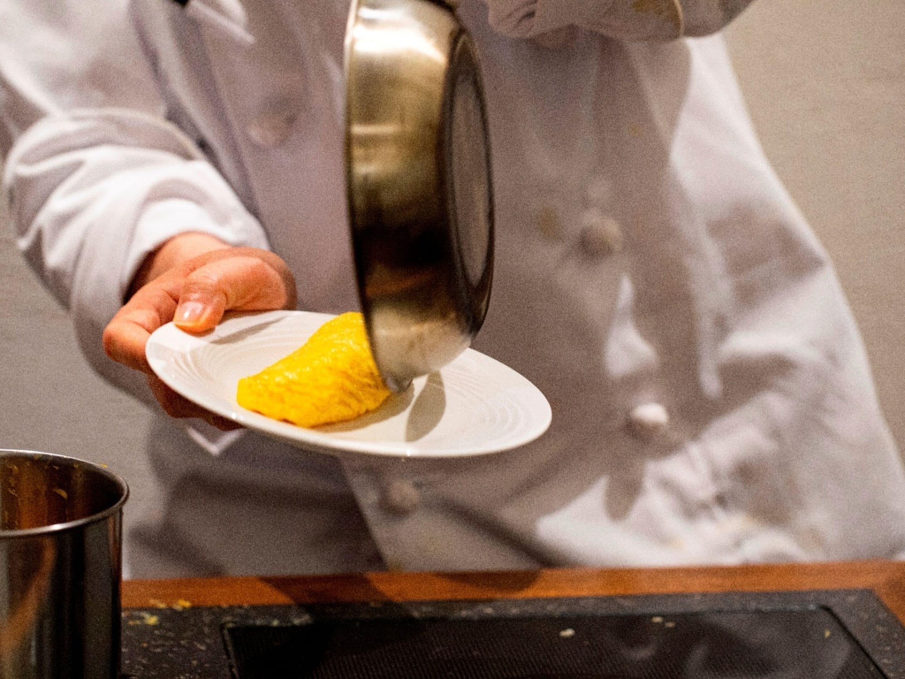 A person in a white coat pouring a yellow substance into a white bowl.