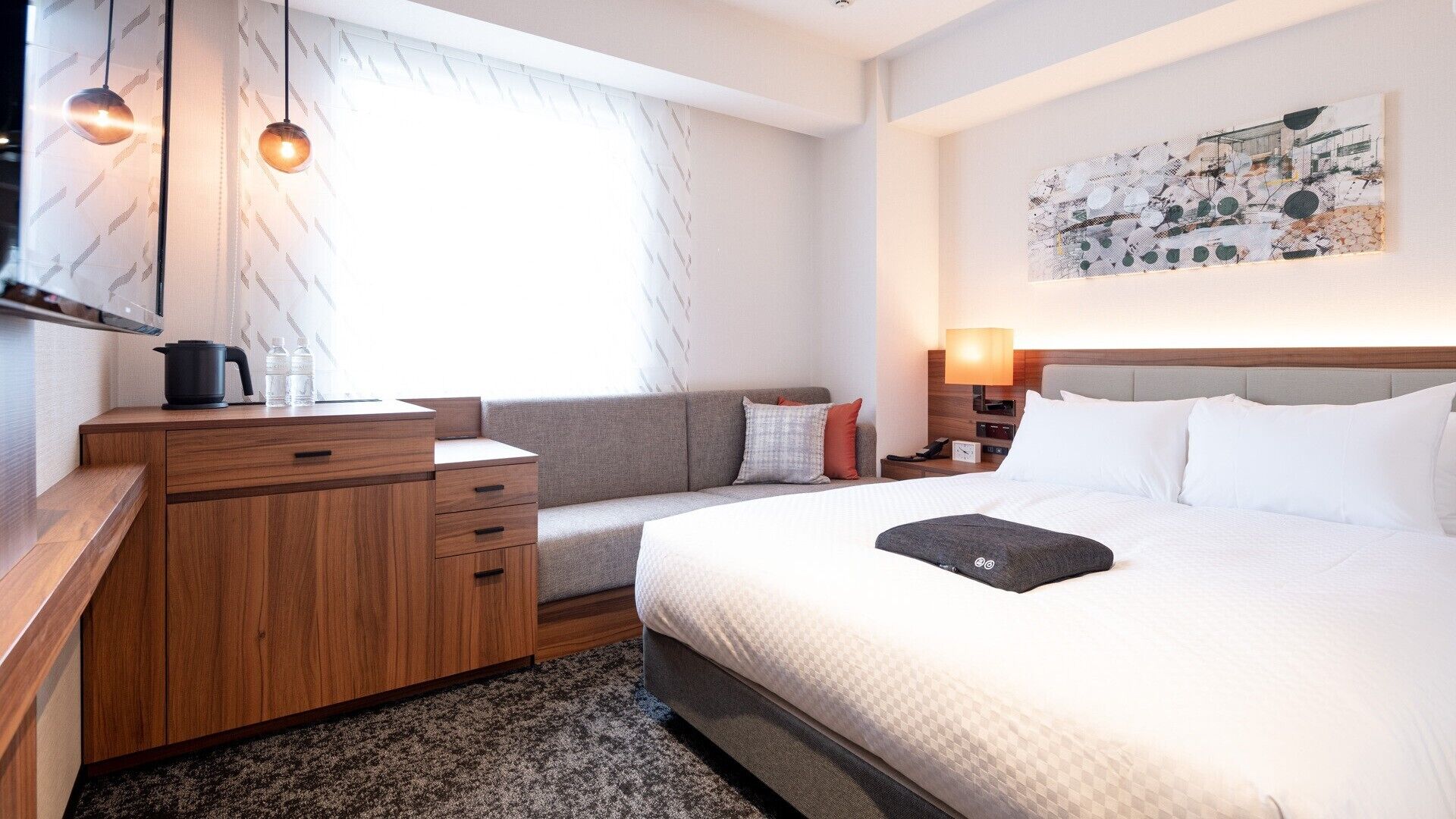 Ein Hotelzimmer mit Bett, Sofa, einem hölzernen Schminktisch, einem Wasserkocher und einem Bild an der Wand.