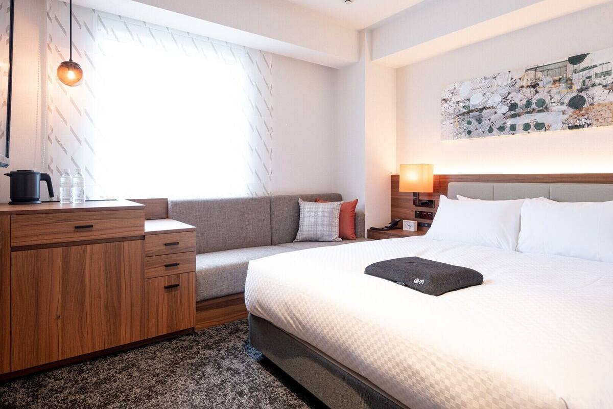 Ein Hotelzimmer mit Bett, Sofa, einem hölzernen Schminktisch, einem Wasserkocher und einem Bild an der Wand.