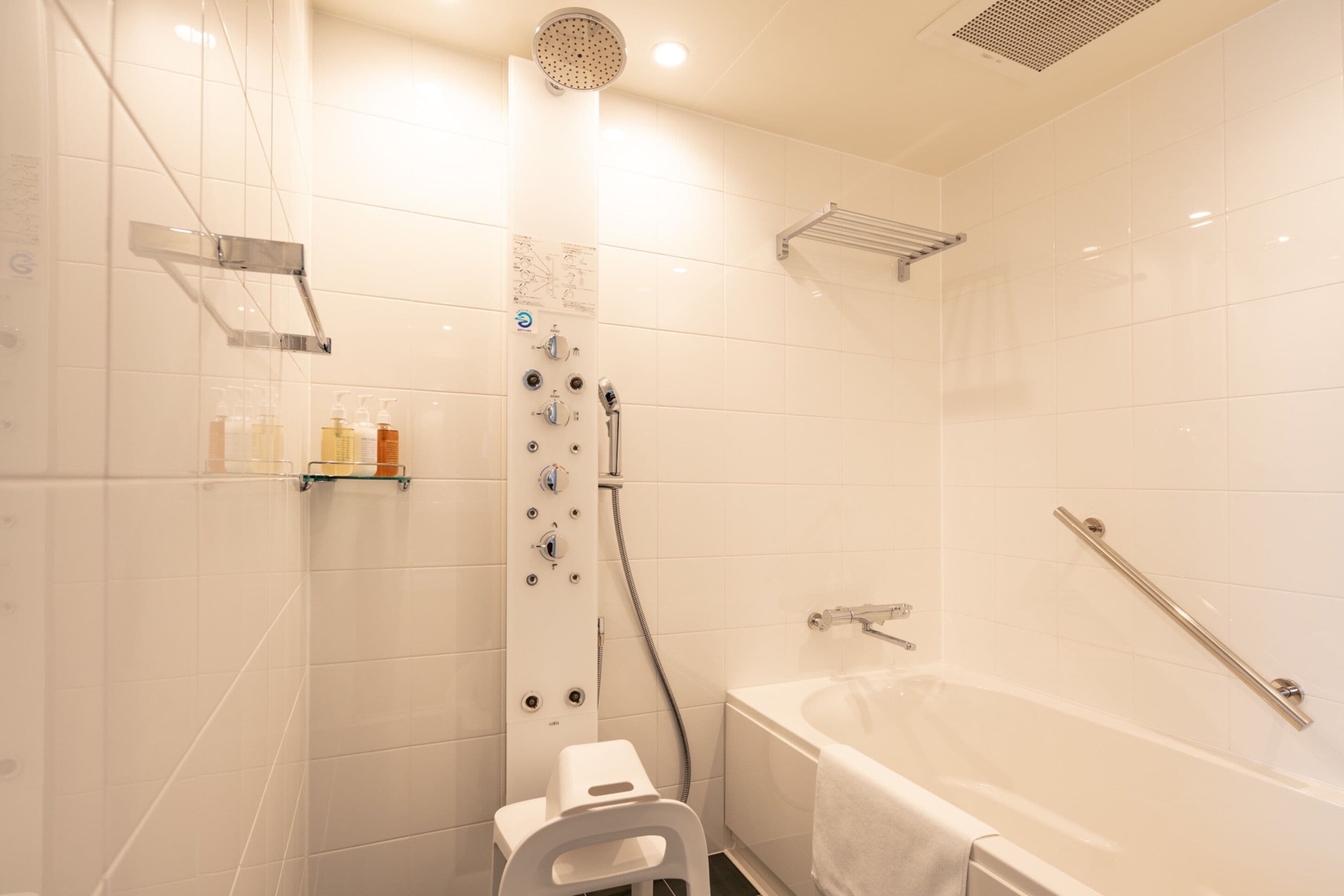 Une salle de bain moderne avec une douche à l’italienne, une baignoire équipée d’une barre d’appui et un petit tabouret.