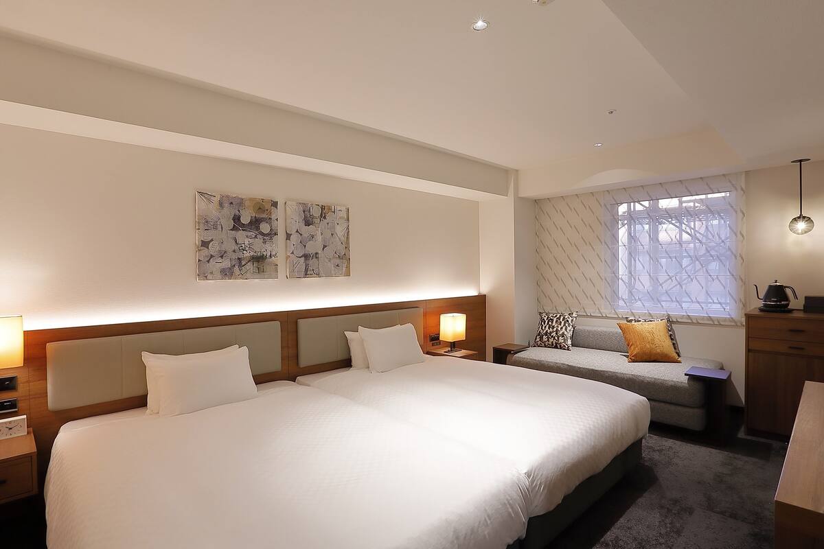 A hotel room with a large bed, a sofa, a desk, and a window with patterned curtains.