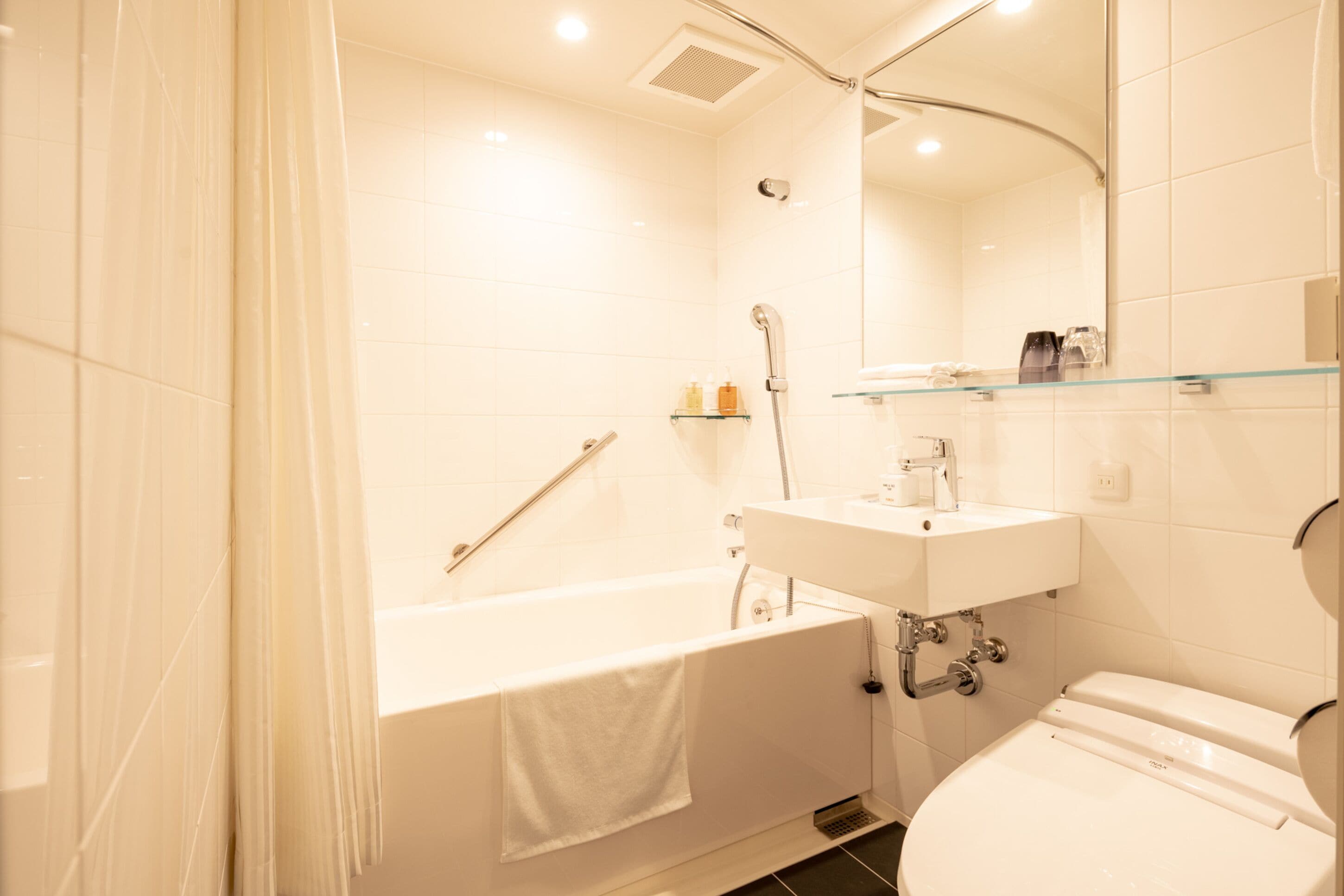 Une salle de bain moderne avec une baignoire, des toilettes et une étagère en verre au-dessus du lavabo.