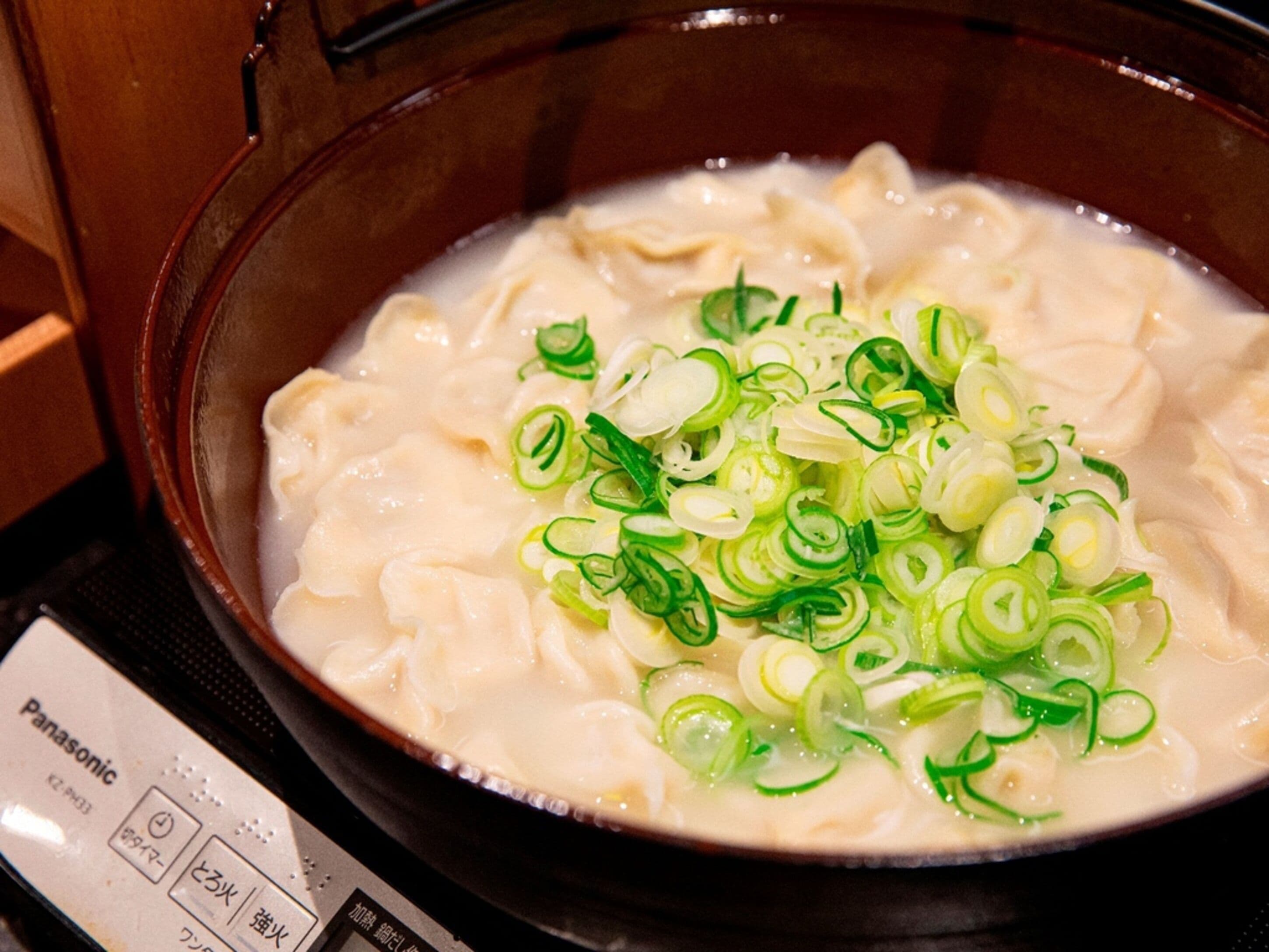 A bowl of soup with dumplings and sliced green onions.