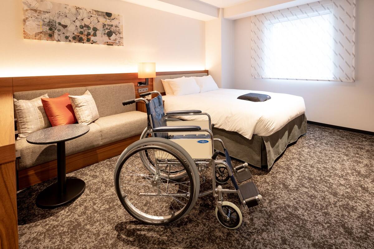 A hotel room with a wheelchair, a sofa, a small table, and a bed.