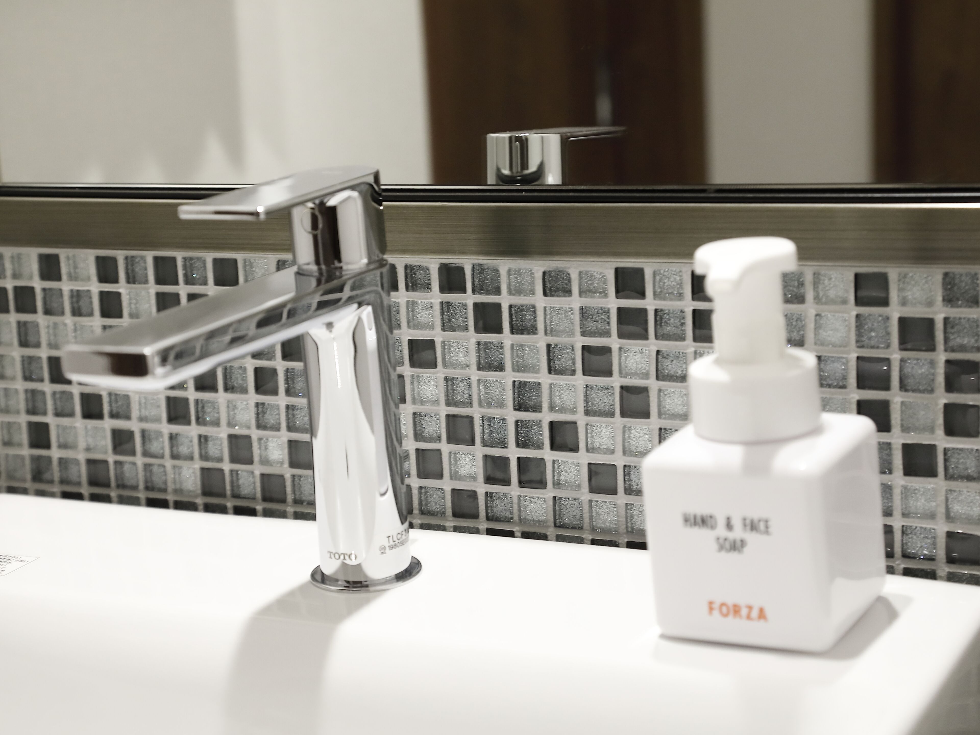 A bathroom sink with a chrome faucet and a bottle of hand and face soap.