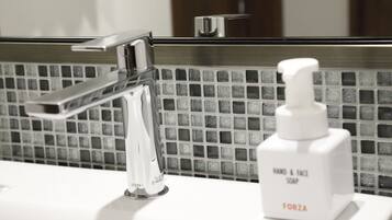 A bathroom sink with a chrome faucet and a bottle of hand and face soap.