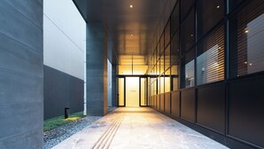 A modern building corridor with a glass facade, a concrete floor, and a pathway leading to an entrance. - Hotel Forza Hakataeki Chikushi - Guchi II (Fukuoka)