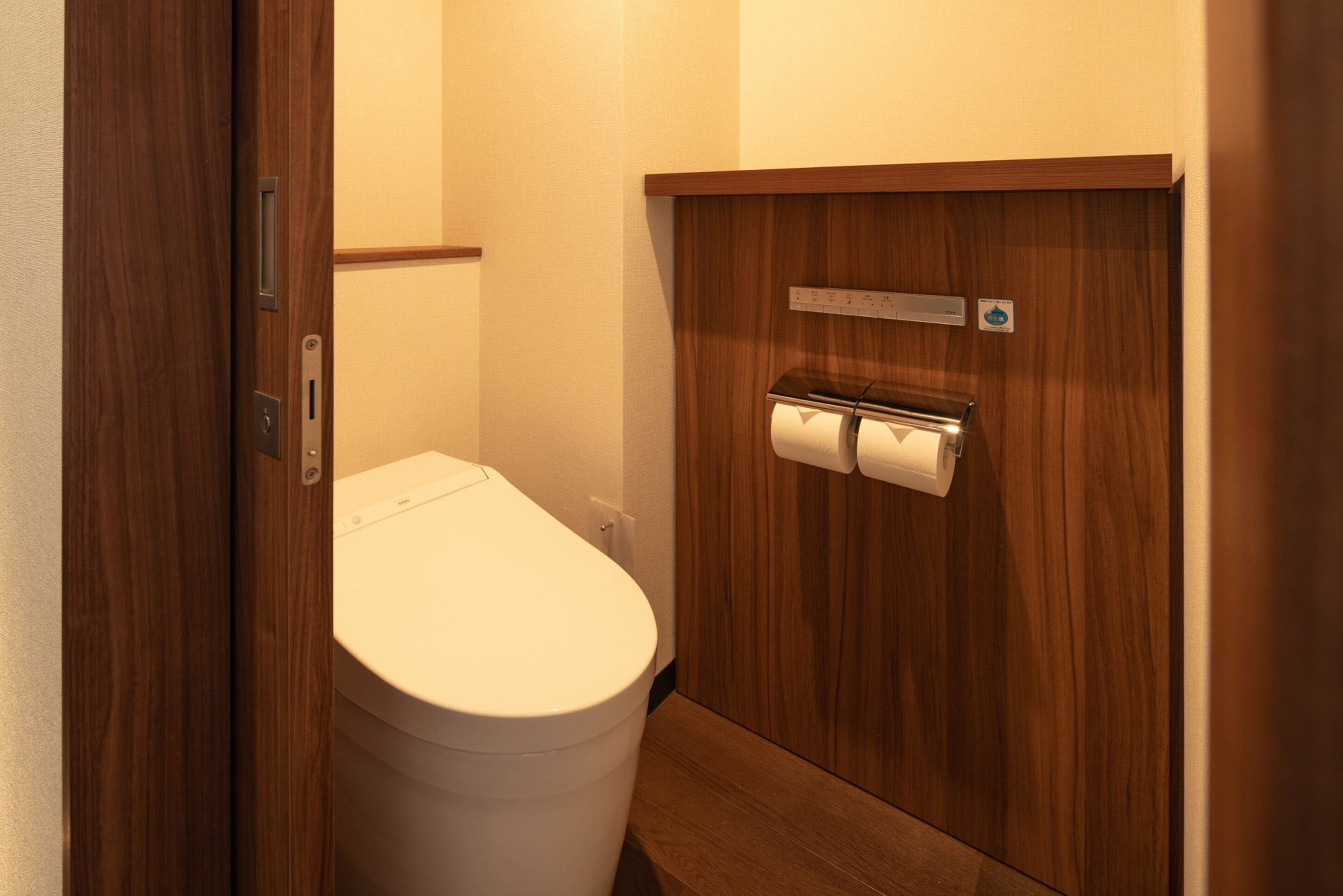 A small, compact bathroom with a wooden vanity, a toilet, and a paper towel dispenser.