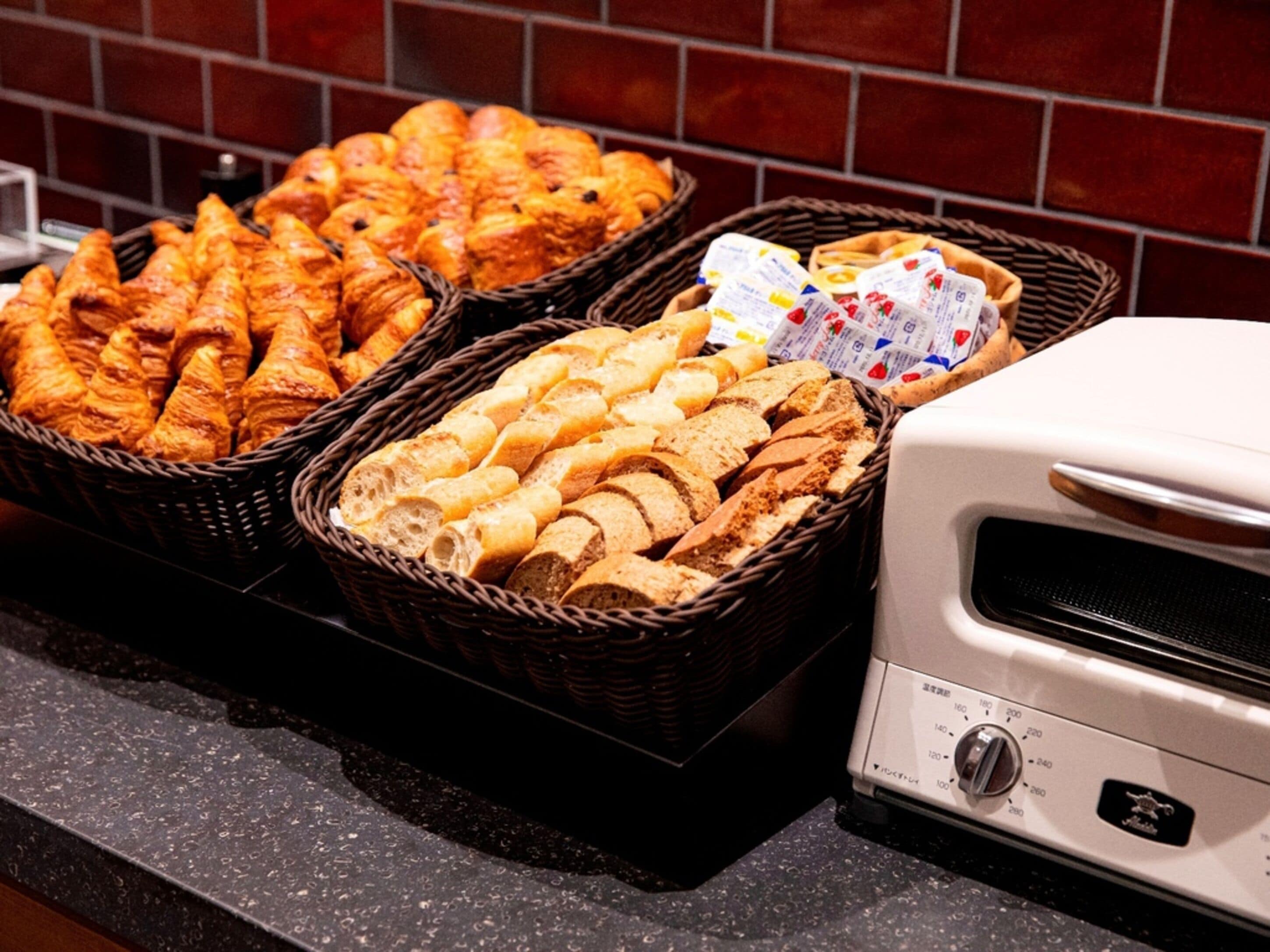 A buffet with baskets of bread and pastries, a toaster, and a tiled backsplash.