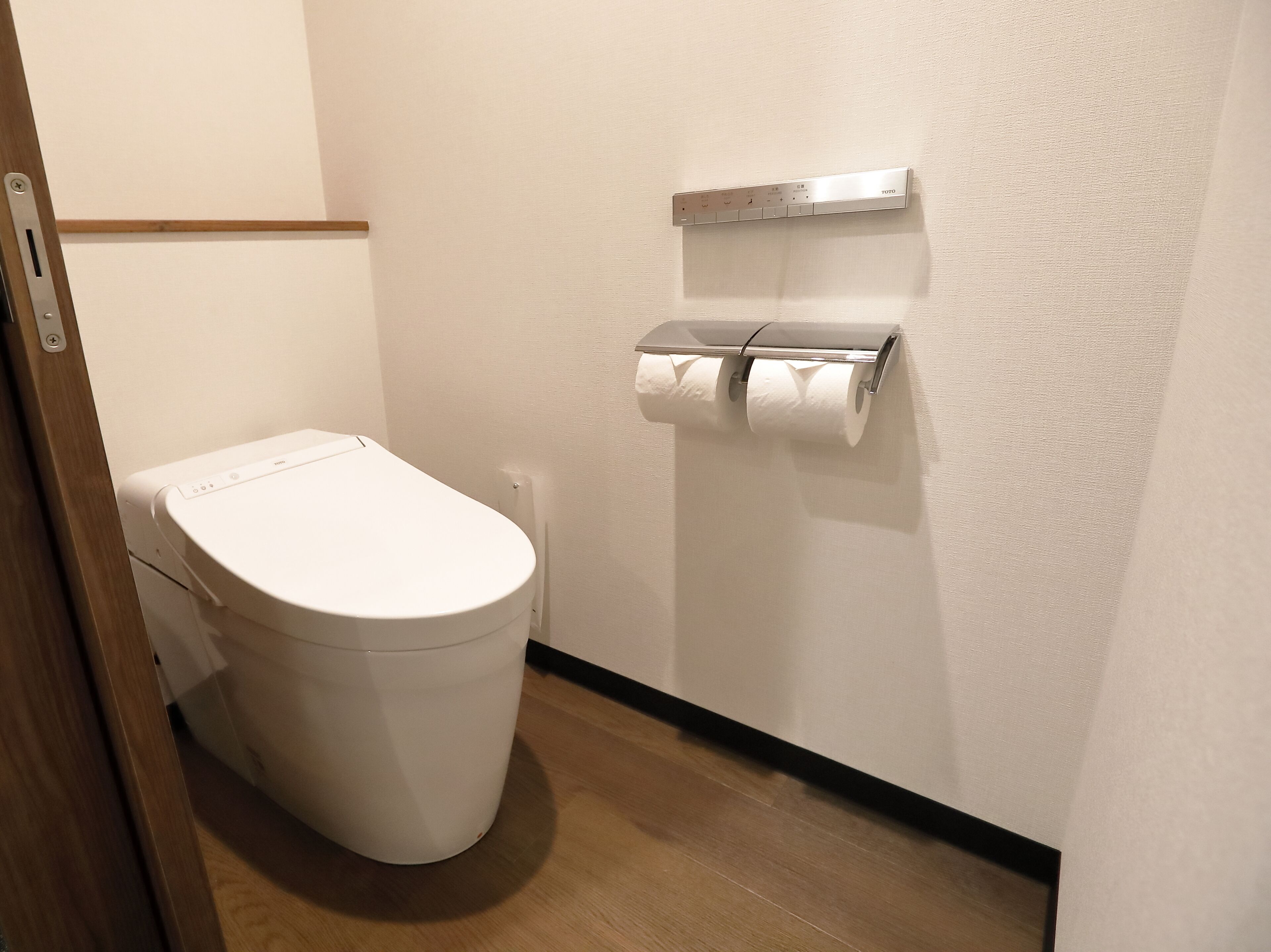 A small, modern bathroom with a white toilet, a toilet paper holder, and a wooden floor.
