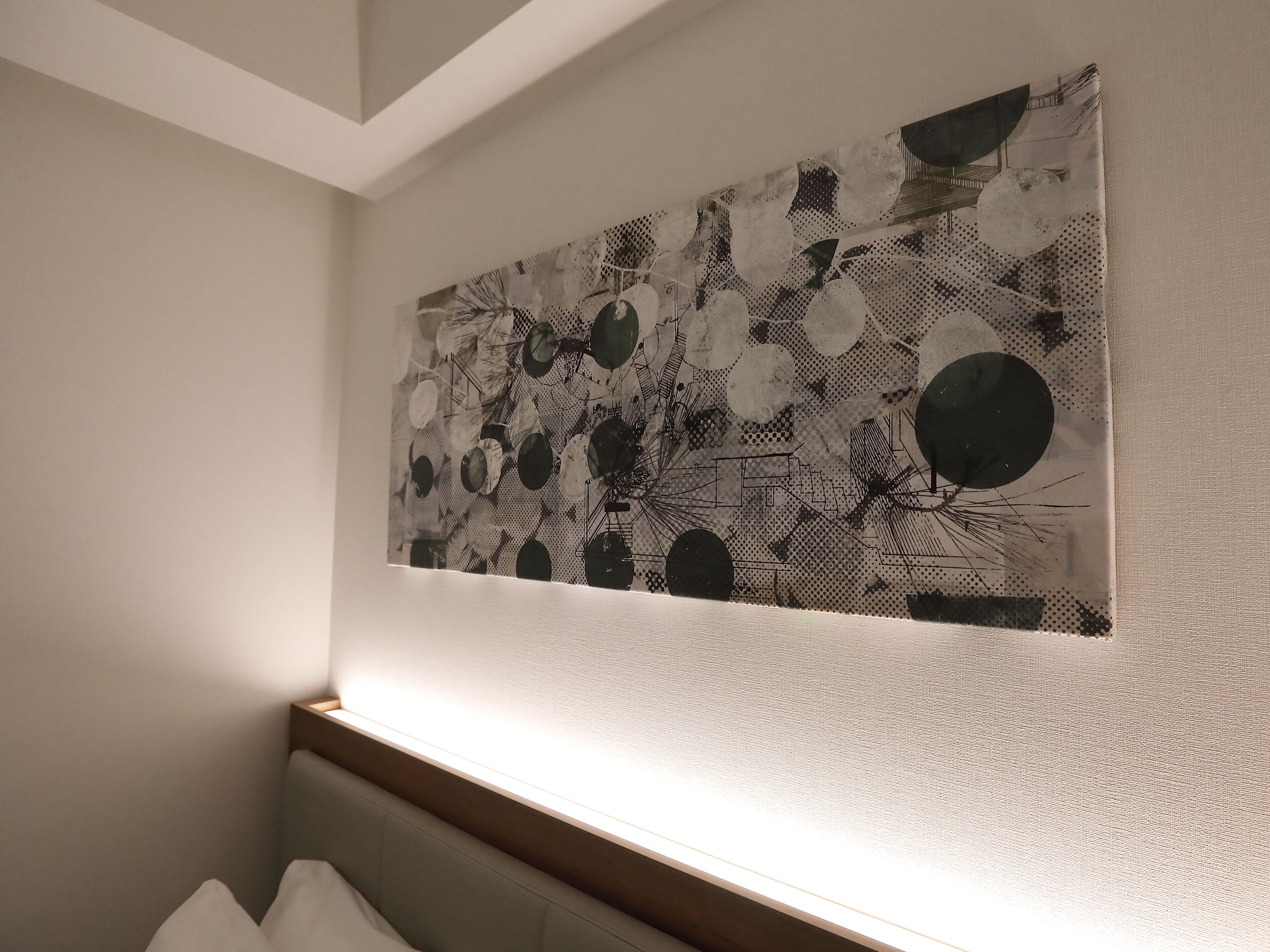Una habitación de hotel moderna con un cuadro abstracto grande en la pared, una cama bien hecha con sábanas blancas y un cabecero de madera.