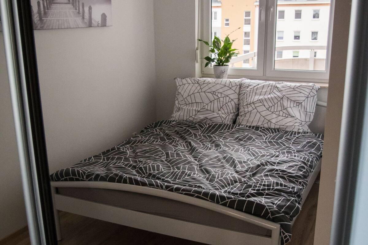 Quarto com cama, janela, planta e pintura na parede.
