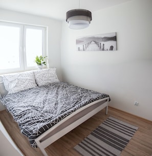Ein Schlafzimmer mit einem Bett, einem Fenster, einer Pflanze und einem Bild an der Wand.