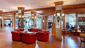 A spacious lobby with a central seating area, wooden columns, and a reception desk. - Maximilian Quellness- und Golfhotel (Bad Griesbach im Rottal)
