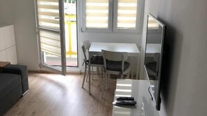 A modern living room with a sofa, a TV mounted on the wall, and a dining area with a table and chairs. - Apartament Przy Skarpie (Torun)