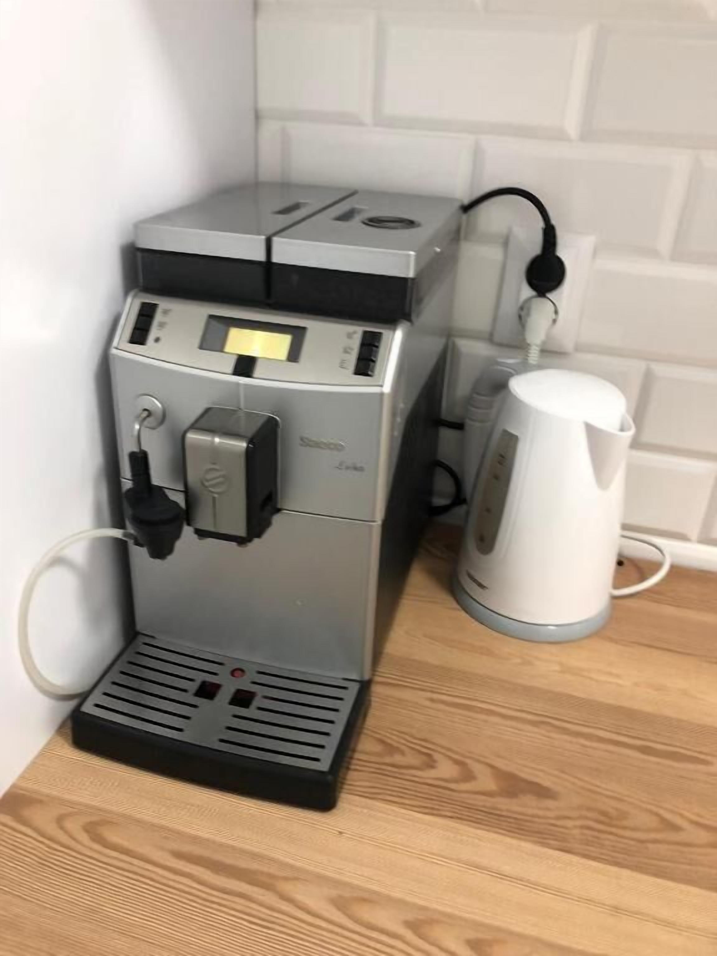 Eine Kaffeemaschine mit Bedienfeld und ein weißes Wasserkocher auf einer Holzauslage.