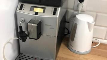 Eine Kaffeemaschine mit Bedienfeld und ein weißes Wasserkocher auf einer Holzauslage.