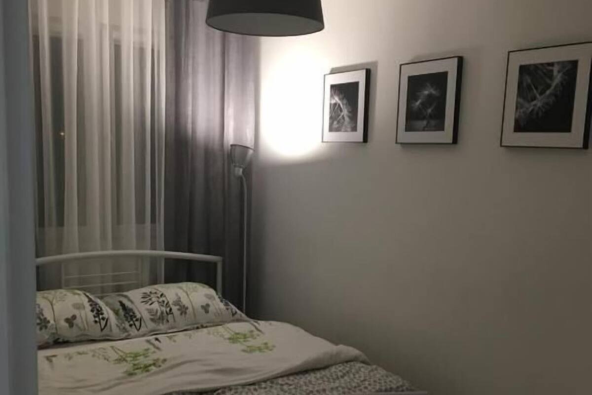 A bedroom with a bed, a hanging lamp, and three framed pictures on the wall.