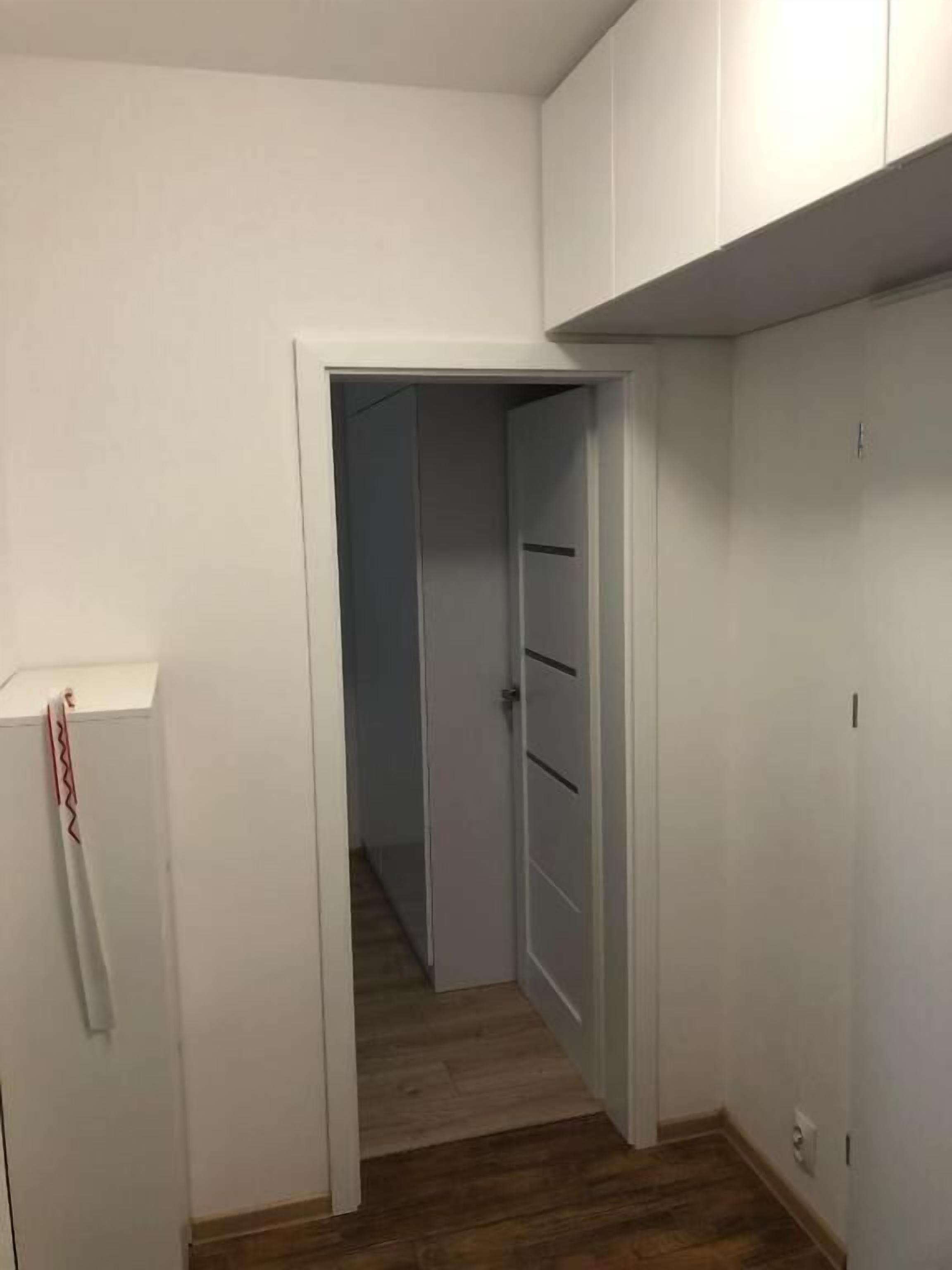 A narrow hallway with a wooden floor leading to a door with a white door frame.