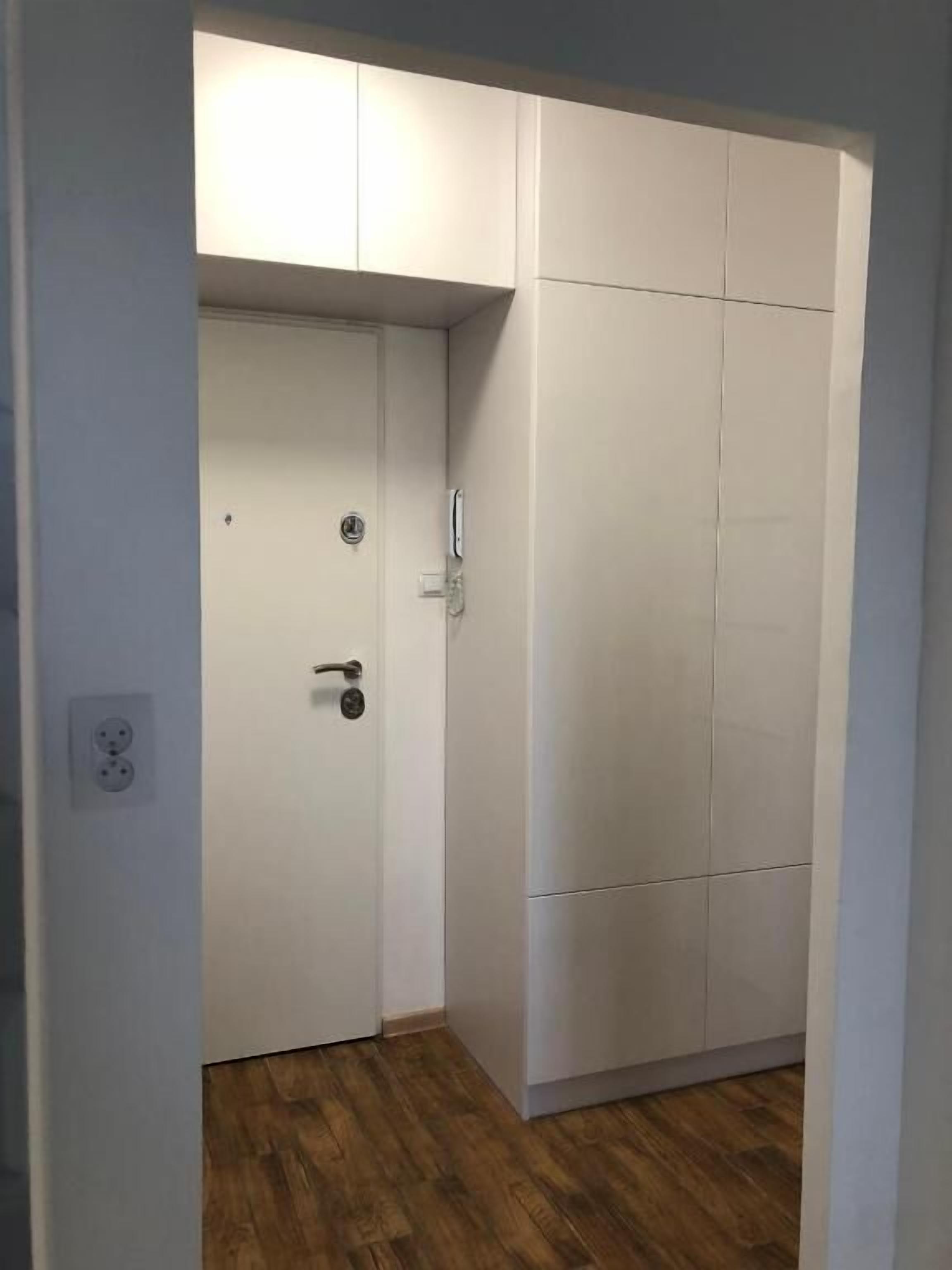 Ein Zimmer mit Holzboden, einer weißen Tür und einem weißen Kleiderschrank mit mehreren Fächern.