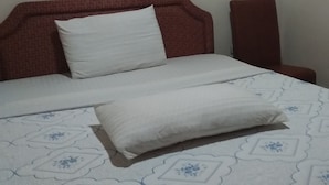 A bed with a patterned bedspread and two pillows, a red headboard, and a red chair against a plain wall. - Plata Guest House (Kigali)