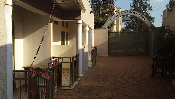 A gated entrance with a sign reading "Than ks & we come again" and a paved pathway leading to a building with columns. - Plata Guest House (Kigali)