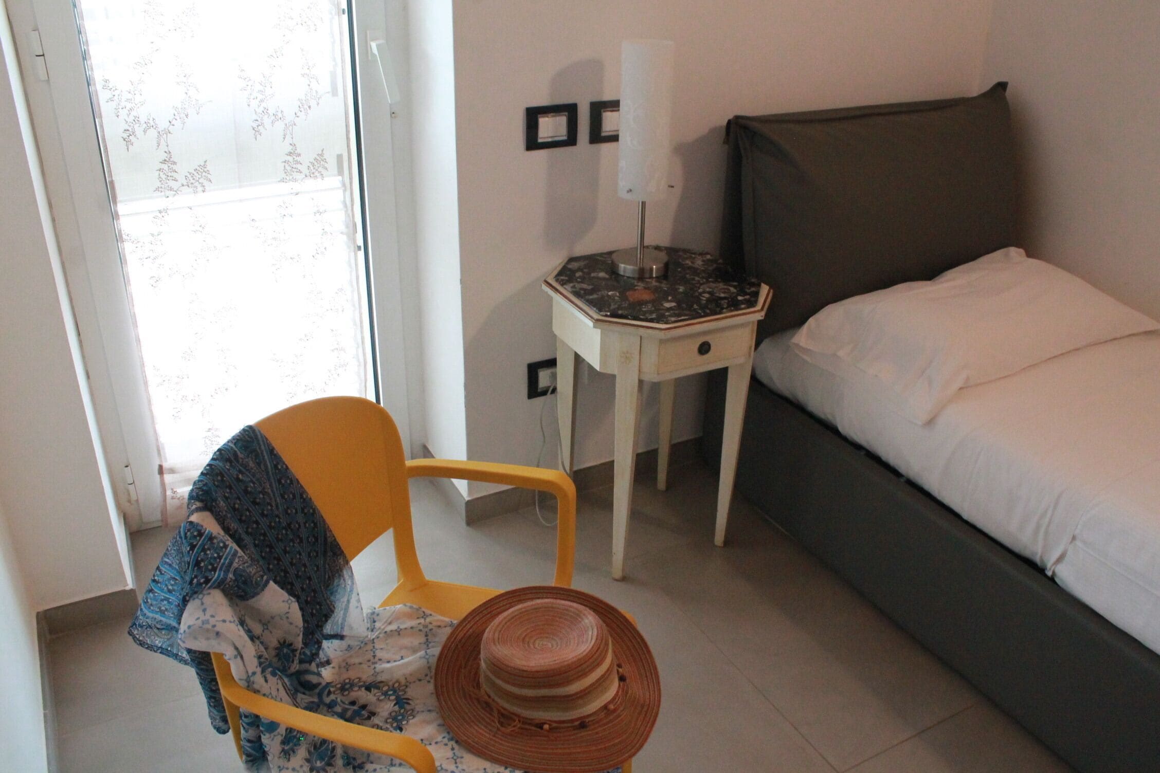 A bedroom with a bed, a nightstand, a chair, and a window.