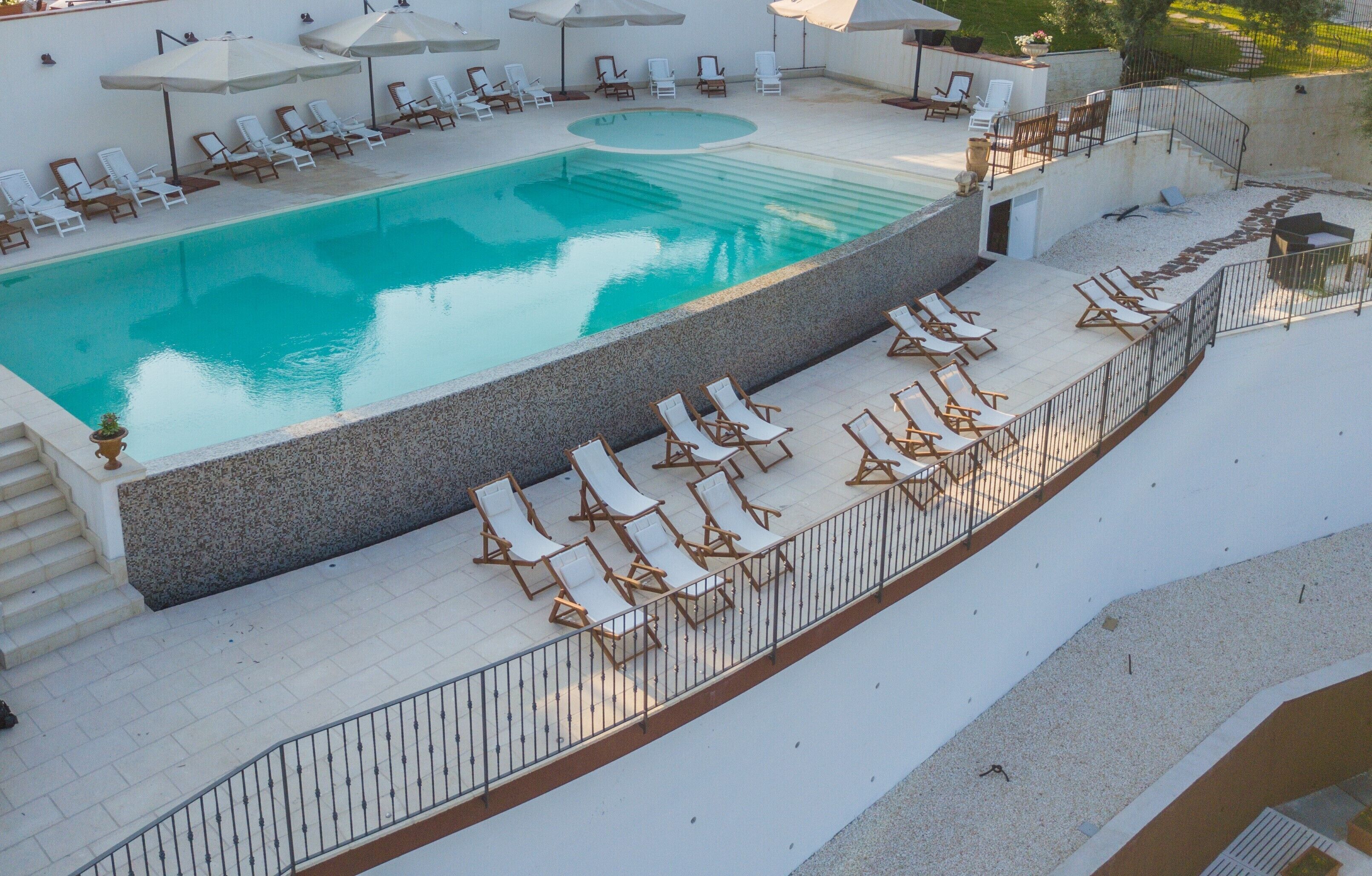 Una piscina sul tetto con diversi lettini e ombrelloni, circondata da un muro in pietra e un parapetto in metallo.