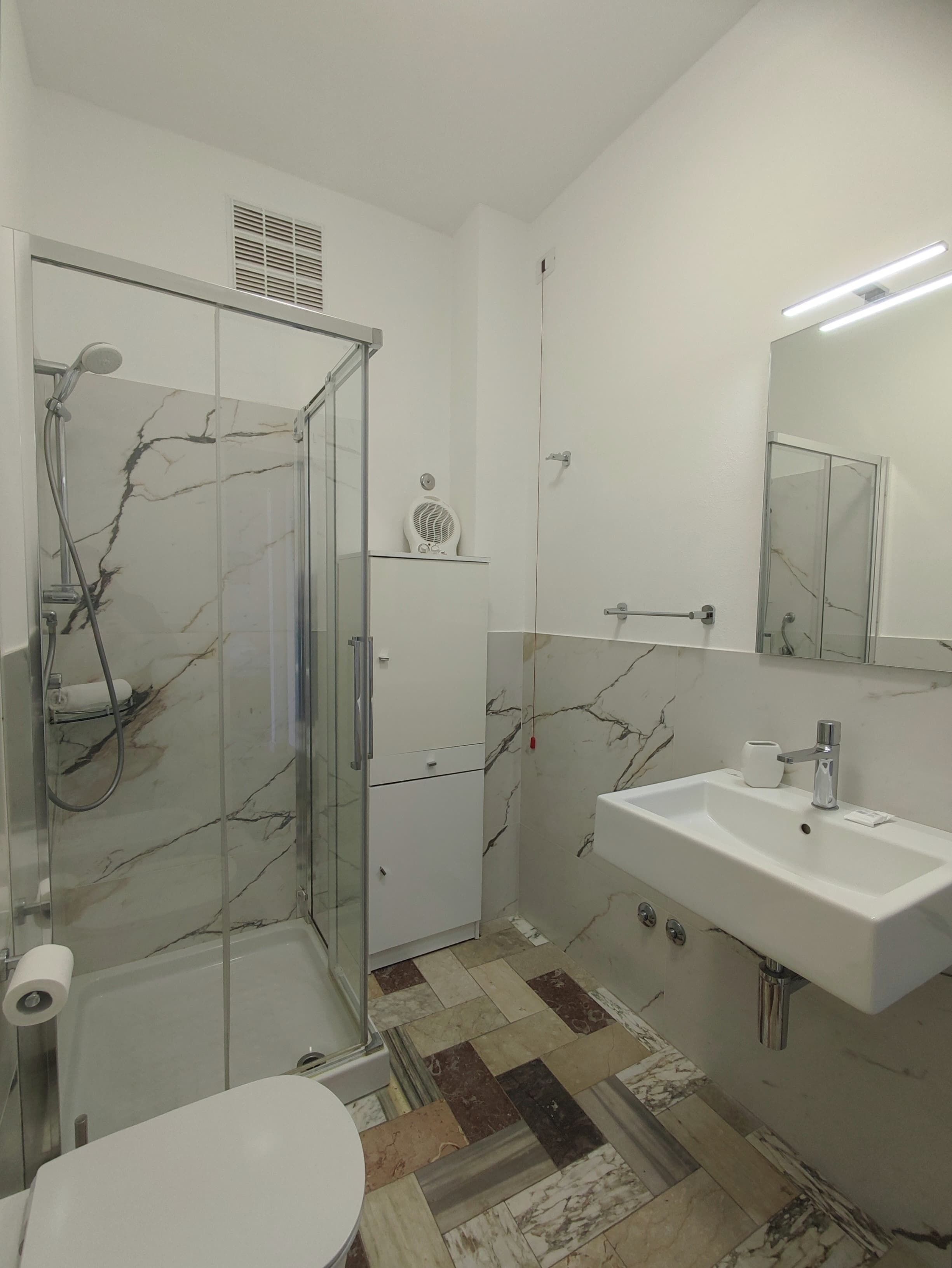 Un baño moderno con ducha envuelta en vidrio, un lavamanos blanco y un suelo con diseño de mármol.