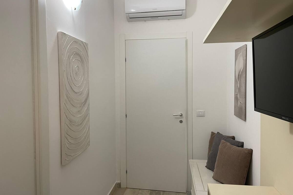 Un couloir avec une porte blanche, un appareil de climatisation au-dessus, et un téléviseur à écran plat fixé au mur.