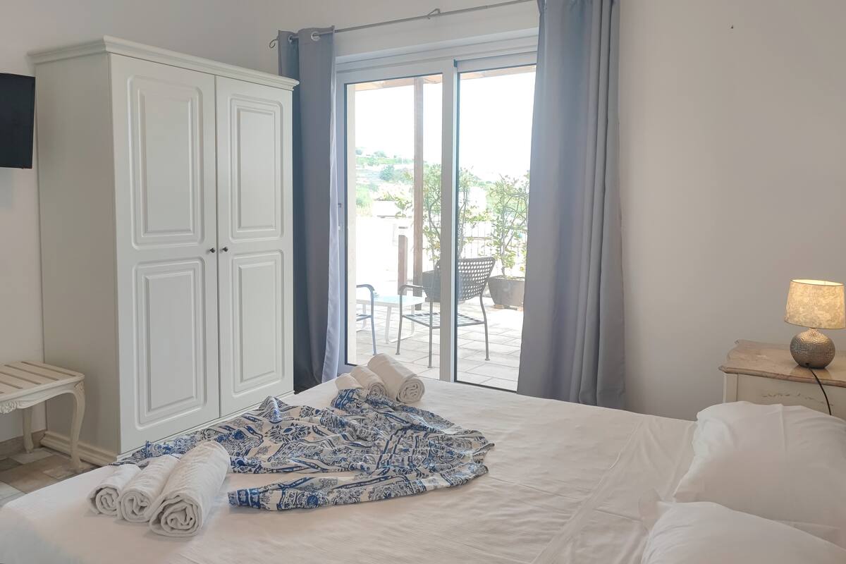 Une chambre avec un lit, une armoire, une télévision, une lampe et une vue sur une terrasse extérieure.