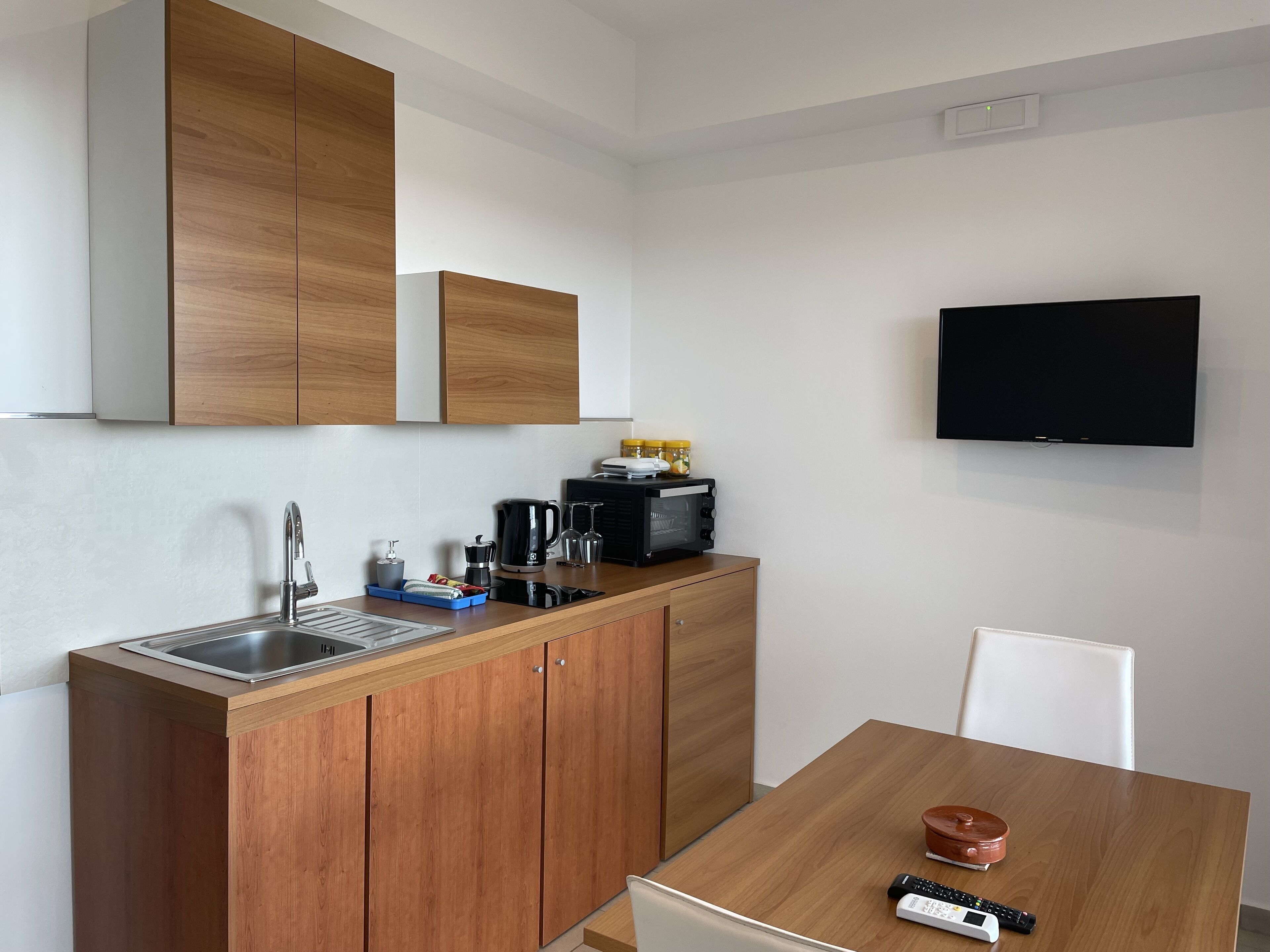 A modern kitchen with wooden cabinets, a built-in sink, and a flat-screen TV mounted on the wall.
