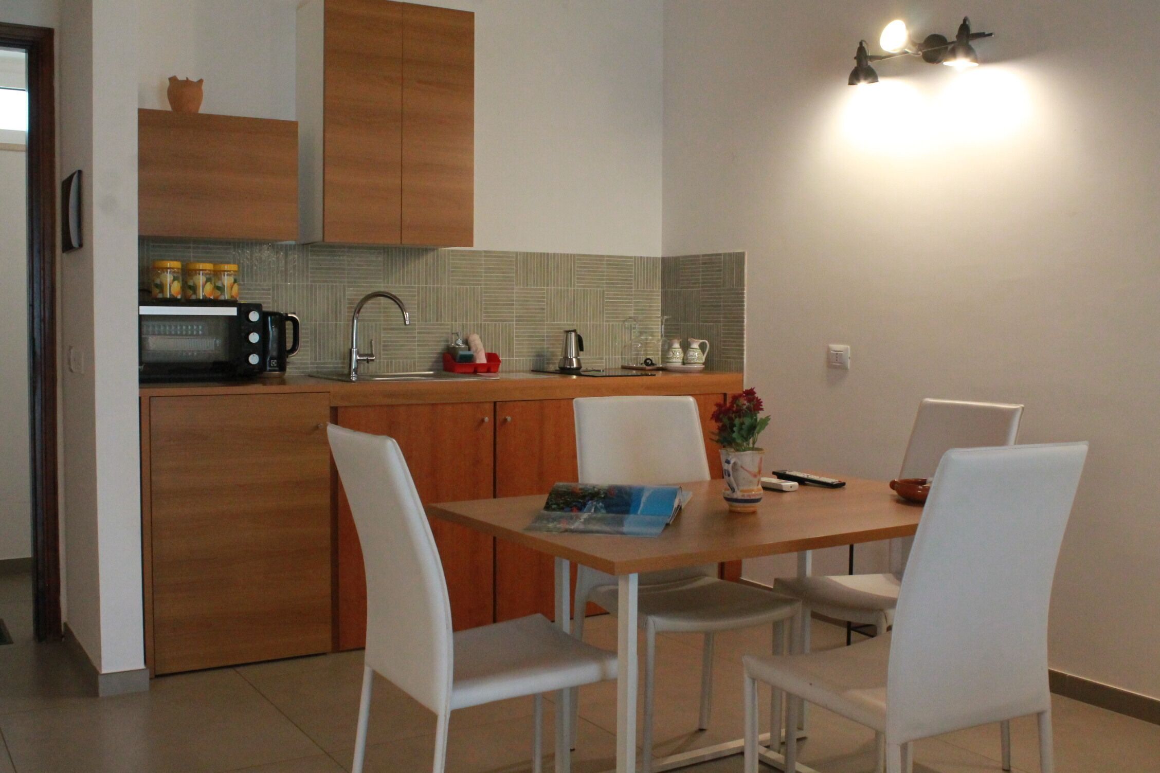 A compact kitchen with wooden cabinets, a microwave, and a sink. There is a dining table with chairs and a vase with flowers.