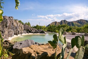 Une piscine naturelle entourée de rochers et de cactus, avec des montagnes en arrière-plan.