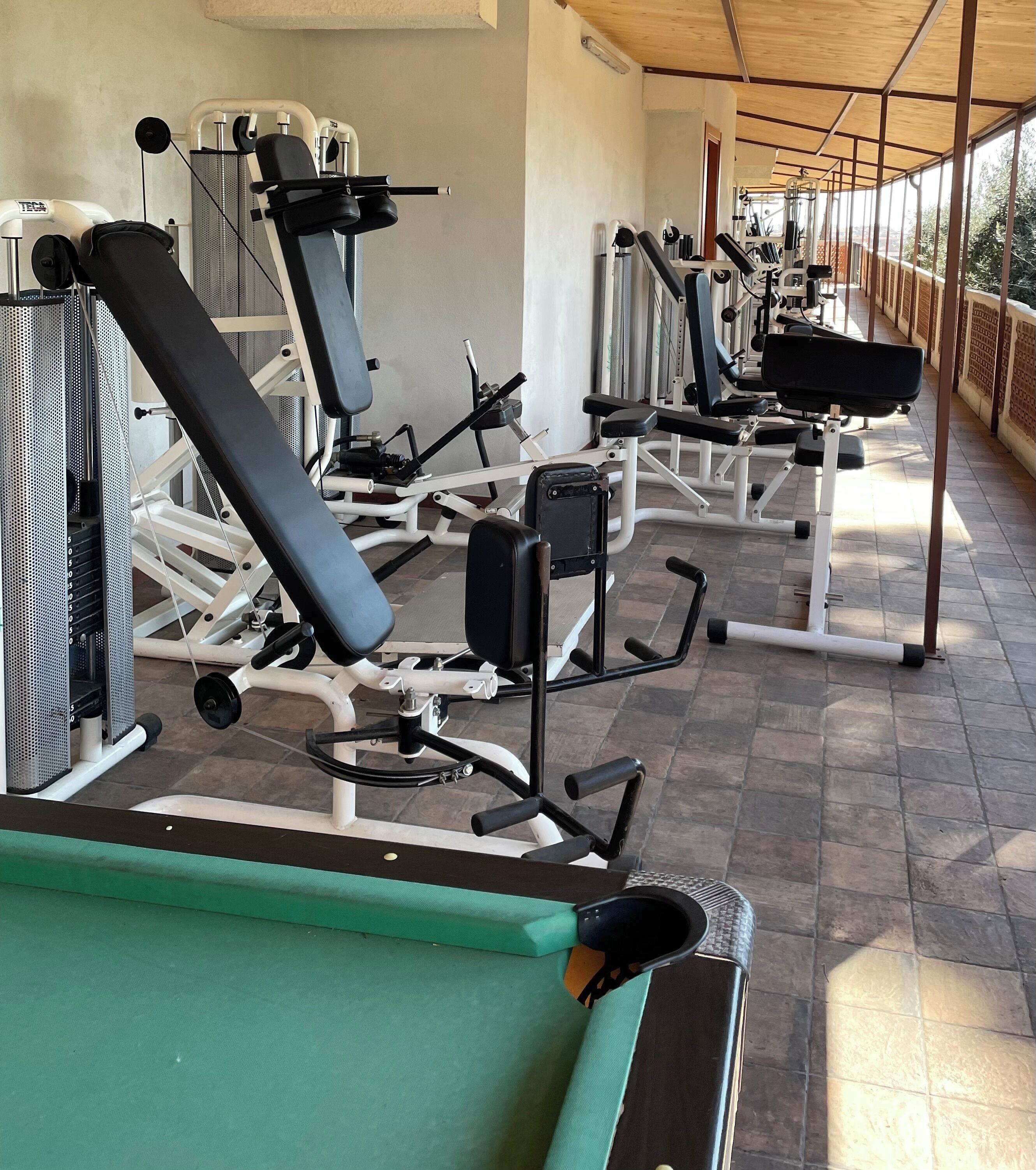 Ein Fitnessstudio mit verschiedenen Trainingsgeräten, darunter Laufbänder und Gewichte, unter einer Überdachung.