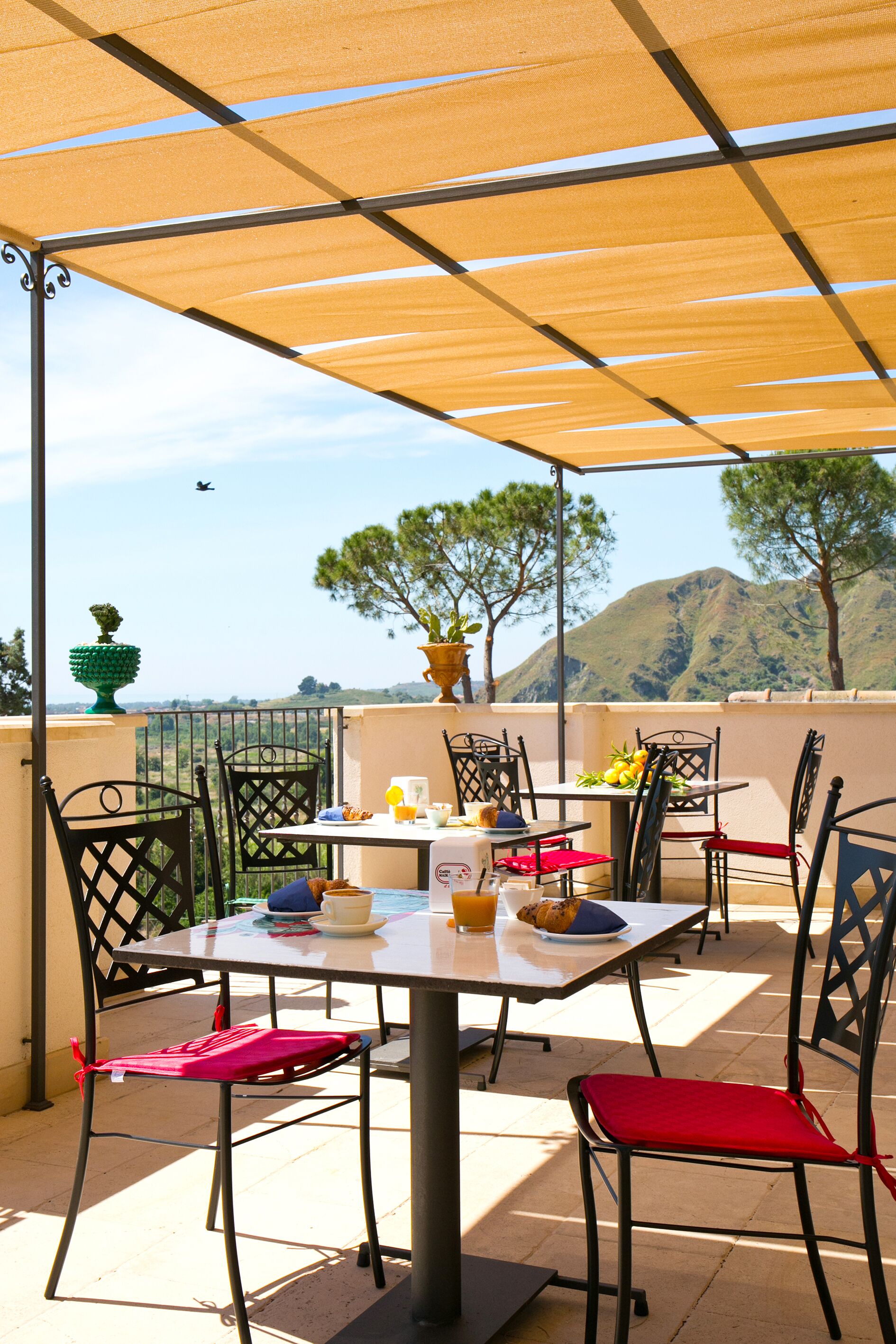 An outdoor patio with a table set for two, surrounded by chairs, and a view of a mountain in the background.
