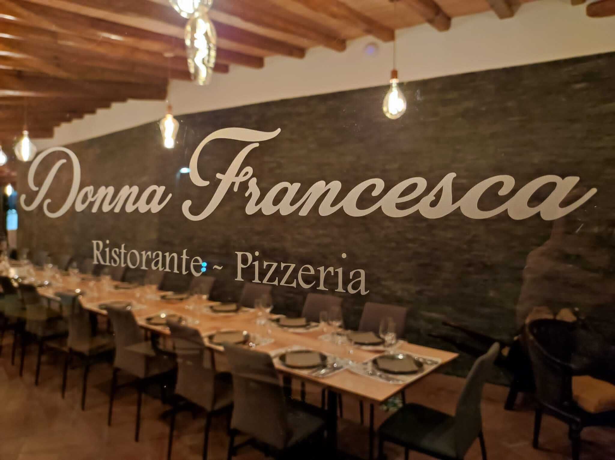 A restaurant interior with tables set for dining, a sign reading "Donna Francesca Ristorante - Pizzeria", and hanging light fixtures.